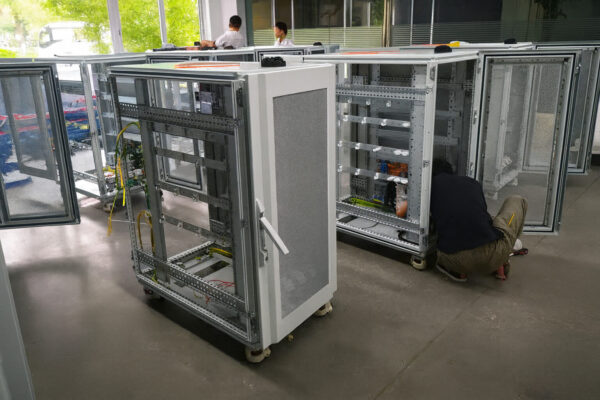 Technician assembling industrial server racks at TPS Elektronik’s production facility, showing multiple open rack systems during the 2015 factory expansion.